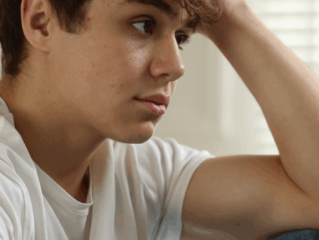 Jeune assis, le regard inquiet et pensif, la tête appuyée sur sa main, exprimant un état de détresse émotionnelle ou de surcharge psychologique.