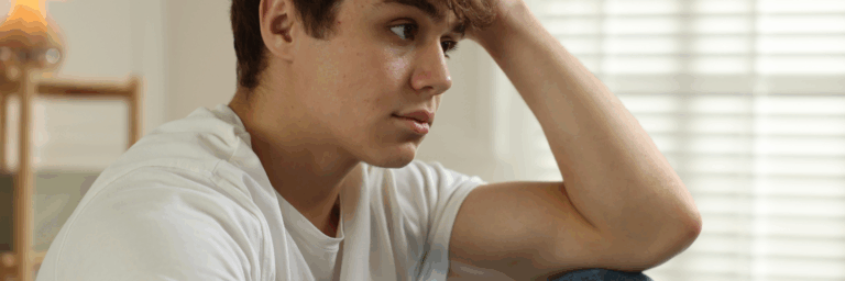 Jeune assis, le regard inquiet et pensif, la tête appuyée sur sa main, exprimant un état de détresse émotionnelle ou de surcharge psychologique.