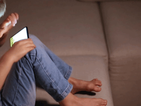 Jeune enfant assis sur un canapé, utilisant un téléphone intelligent, illustrant l’exposition précoce aux écrans chez les tout-petits.