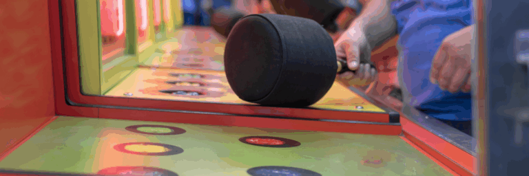 Main tenant un gros marteau rembourré au-dessus des trous colorés d’un jeu de foire où il faut frapper les marmottes qui apparaissent.