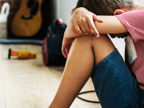 Enfant assis au sol, la tête appuyée sur ses bras, exprimant un moment de détresse ou de peur dans un environnement familial.
