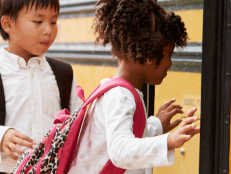 Groupe d’enfants portant des sacs à dos qui montent à bord d’un autobus scolaire jaune.