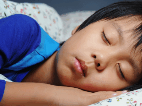 « Enfant endormi paisiblement dans son lit, la tête appuyée sur une taie d’oreiller fleurie.