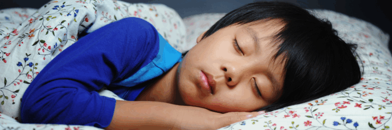 « Enfant endormi paisiblement dans son lit, la tête appuyée sur une taie d’oreiller fleurie.