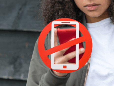 « Une adolescente regarde un téléphone rouge, partiellement caché par un grand symbole d’interdiction de cellulaire, indiquant l’interdiction d’utiliser les téléphones dans les milieux scolaires.
