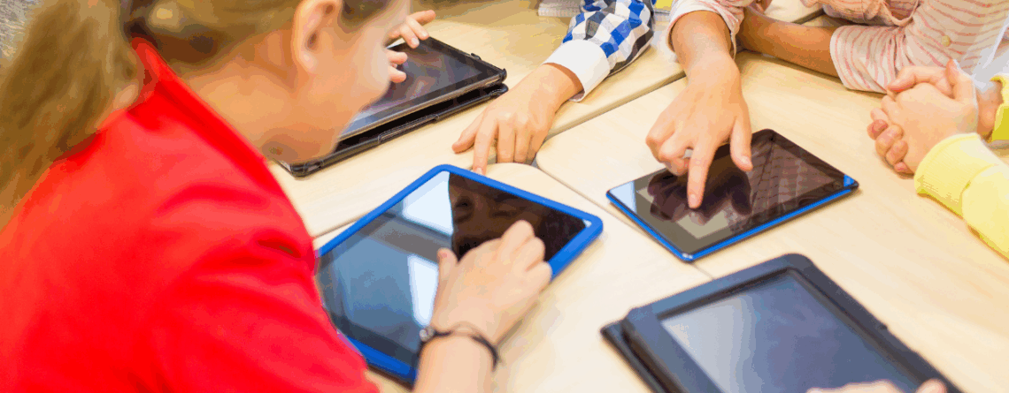 Enfants réunis autour d’une table utilisant des tablettes numériques, illustrant l’exposition aux écrans et les usages numériques chez les jeunes.