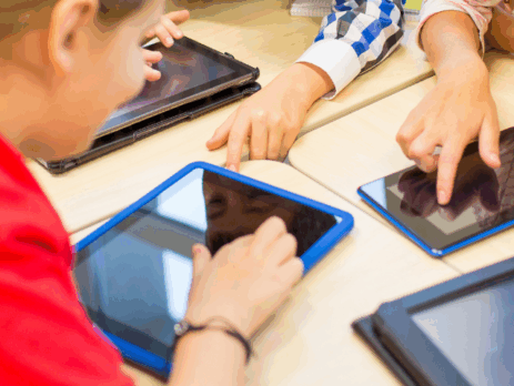 Enfants réunis autour d’une table utilisant des tablettes numériques, illustrant l’exposition aux écrans et les usages numériques chez les jeunes.